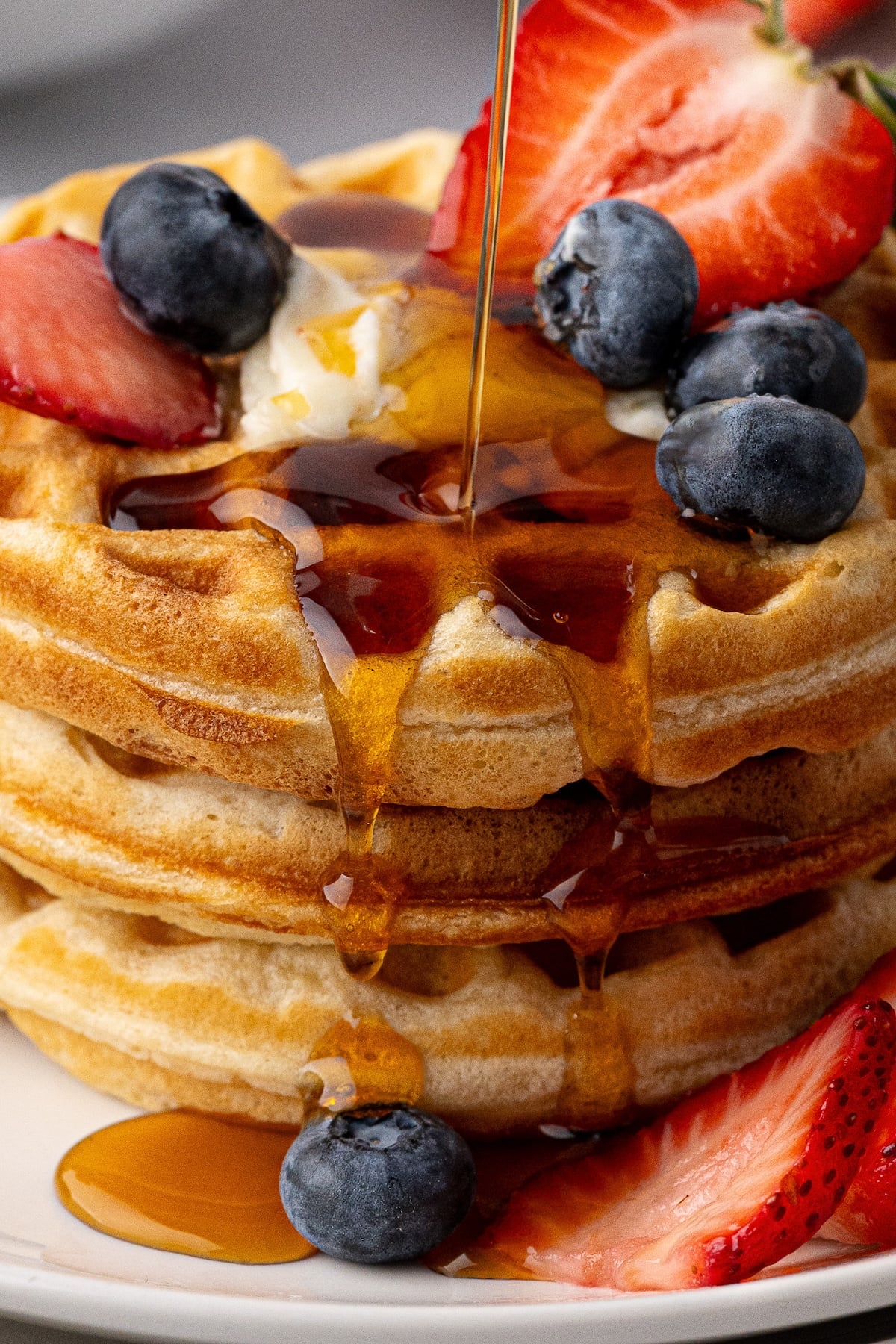 Maple syrup being poured over a stack of thick Southern-style buttermilk waffles.