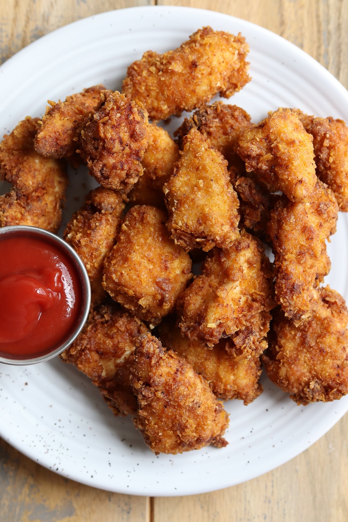 A dinner plate filled with cornflake chicken nuggets and a small bowl of ketchup.