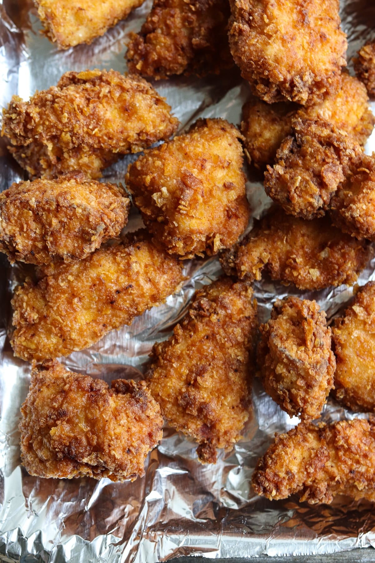 A macro close-up shot of a few pieces of crispy cornflake fried chicken, highlighting the detailed, craggy texture of the crushed cornflake crust.