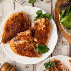 An overhead view of perfectly oven-roasted bone-in split chicken breasts featuring a savory Texas dry rub and golden crispy skin, served on a plate.
