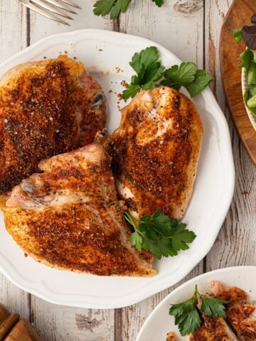 An overhead view of perfectly oven-roasted bone-in split chicken breasts featuring a savory Texas dry rub and golden crispy skin, served on a plate.