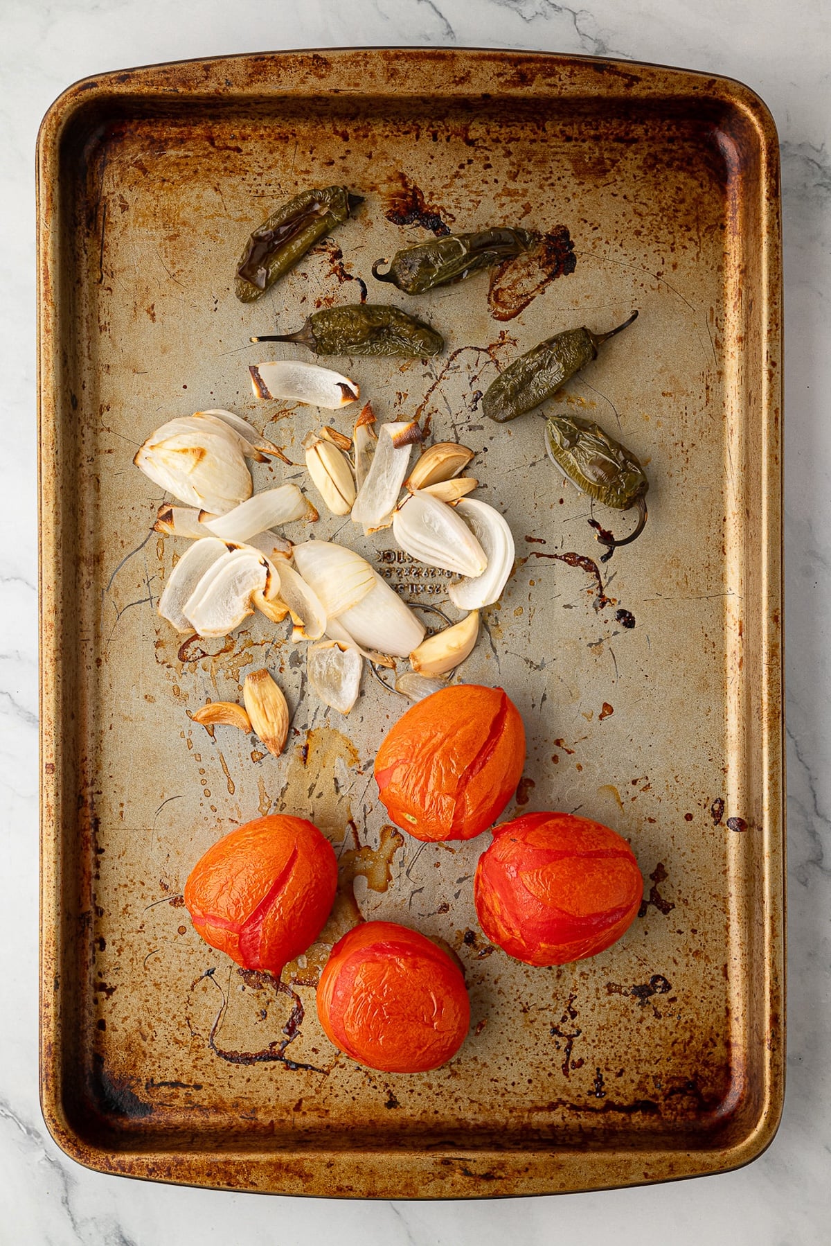 Blistered Roma tomatoes, charred jalapeños, garlic, and onions on a baking sheet.
