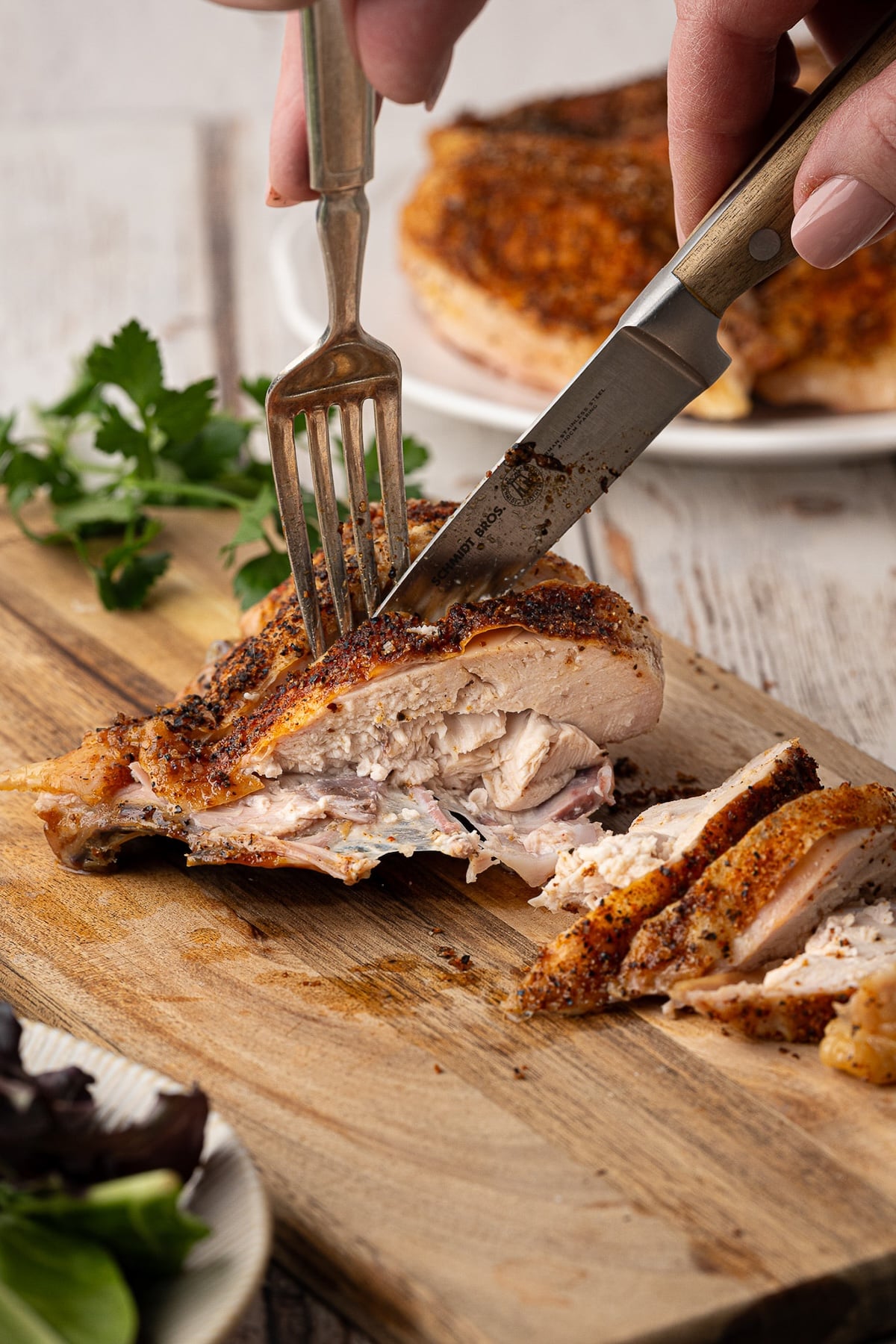 Slicing into the baked bone-in chicken breast on a wood cutting board.