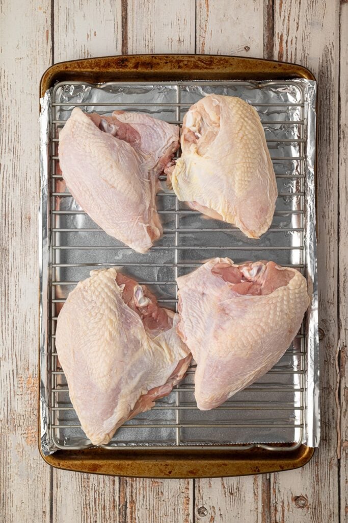 An overhead shot showing how to place the split chicken breasts on a rack fit over a foil lined baking sheet.