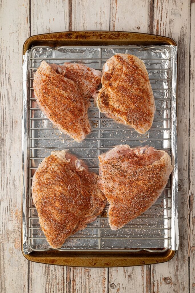 Seasoned bone-in chicken breasts arranged evenly on a lined baking sheet ready to be roasted.