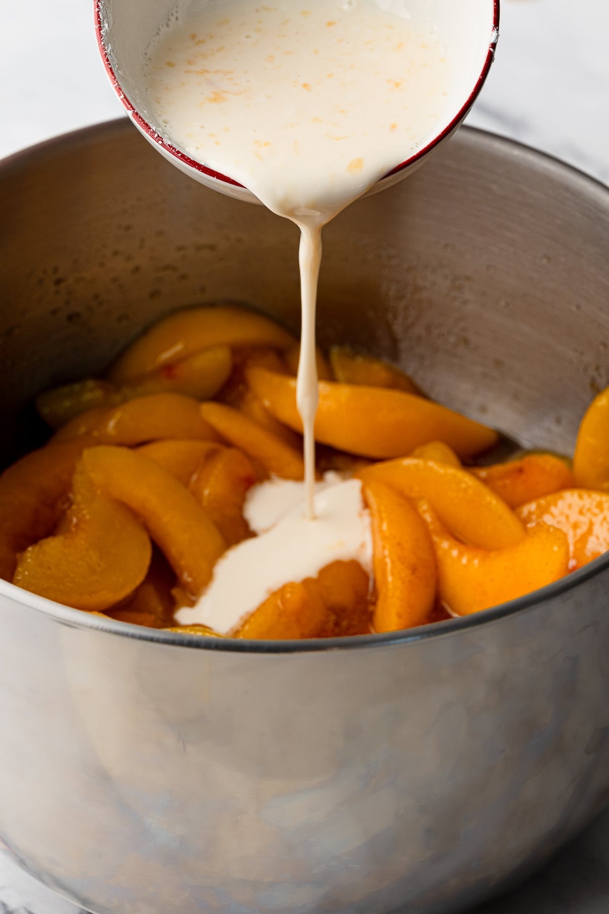 A white cornstarch slurry being poured into a bubbling pot of stovetop peach pie filling to thicken the juices.