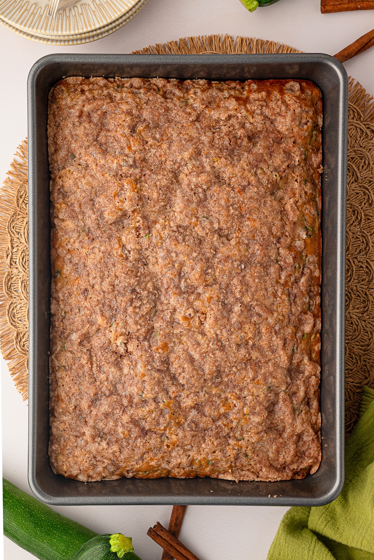 A freshly baked cinnamon zucchini coffee cake straight from the oven, sitting in a metal 9x13 pan with a golden brown, crinkly cinnamon sugar crust.