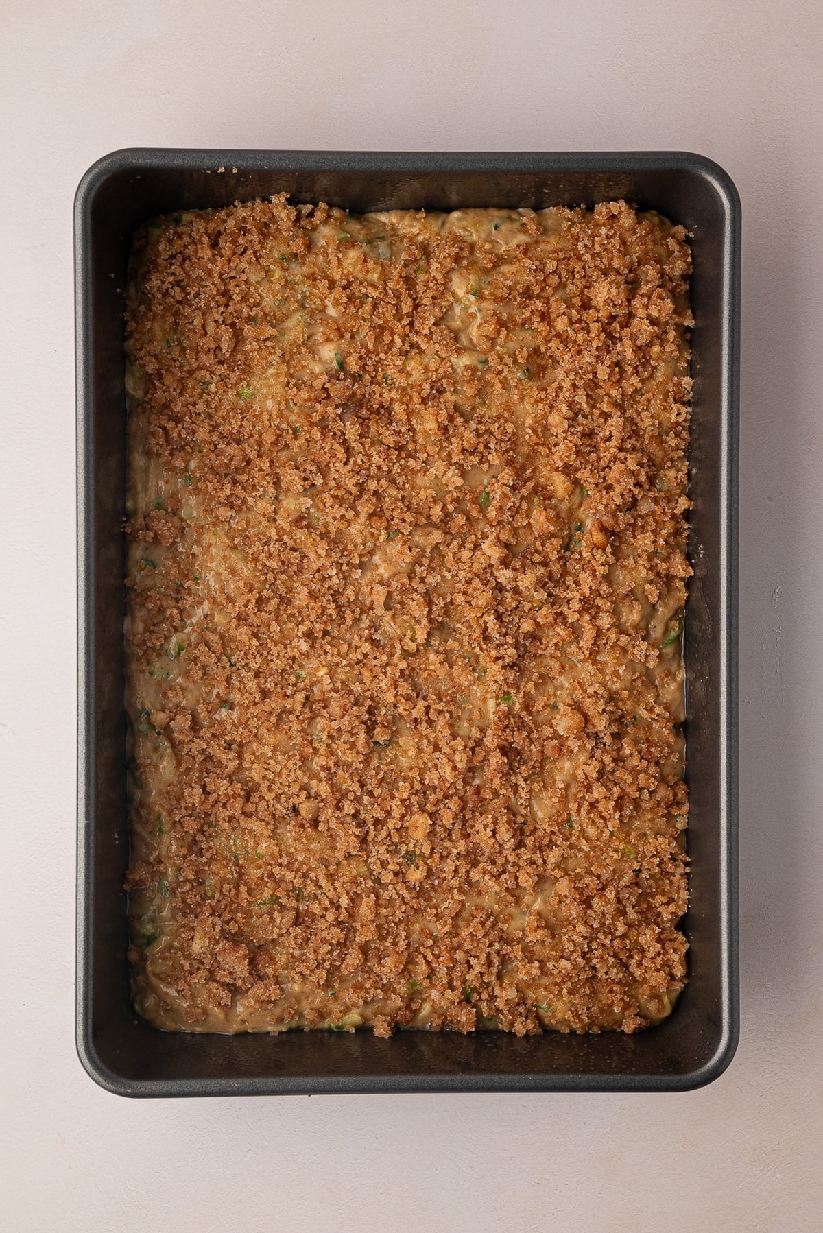 Spreading a layer of zucchini cake batter into a metal 9x13 baking pan and sprinkling the cinnamon sugar mixture evenly over the top.