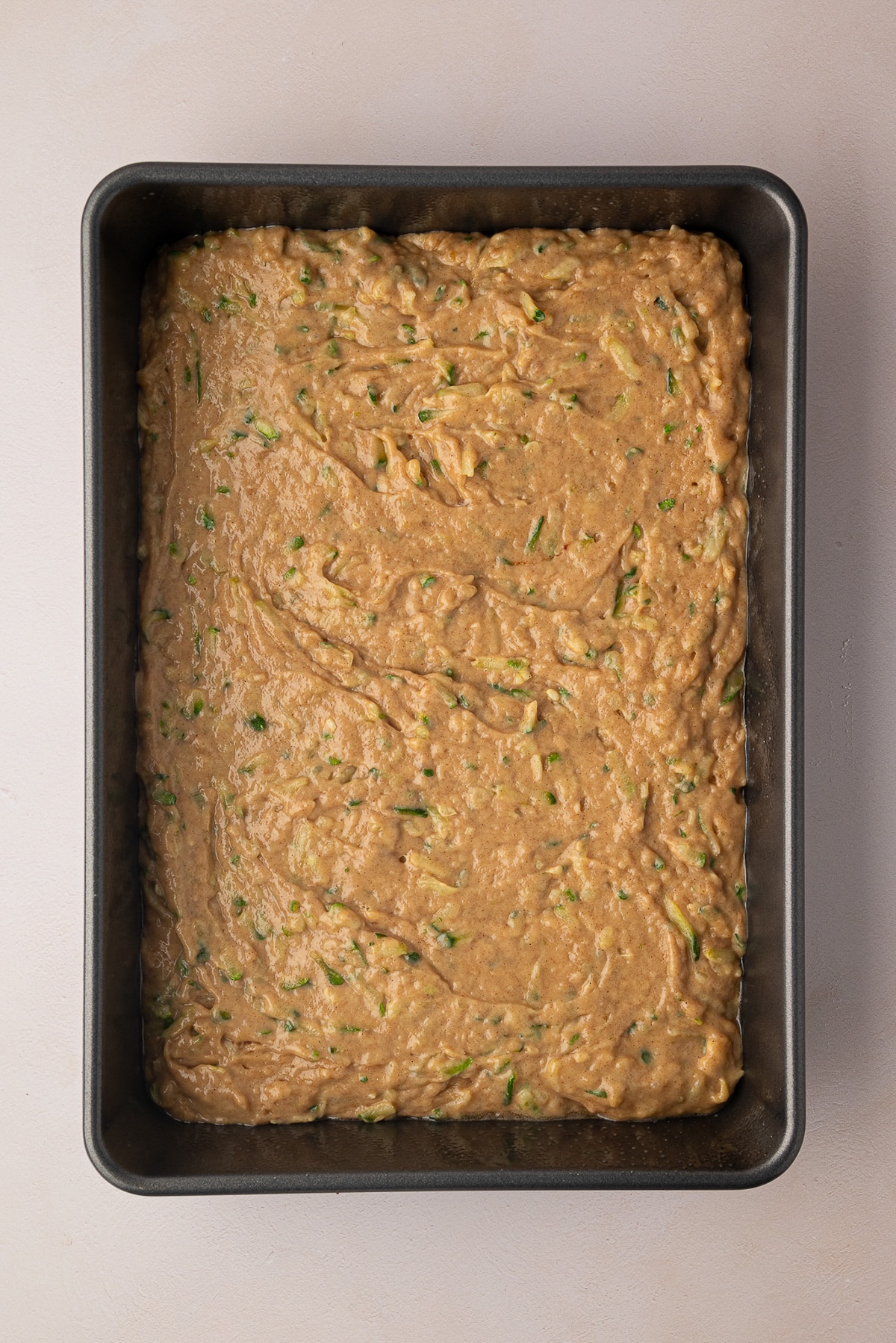 Spreading zucchini cake batter into a 9x13-inch cake pan.