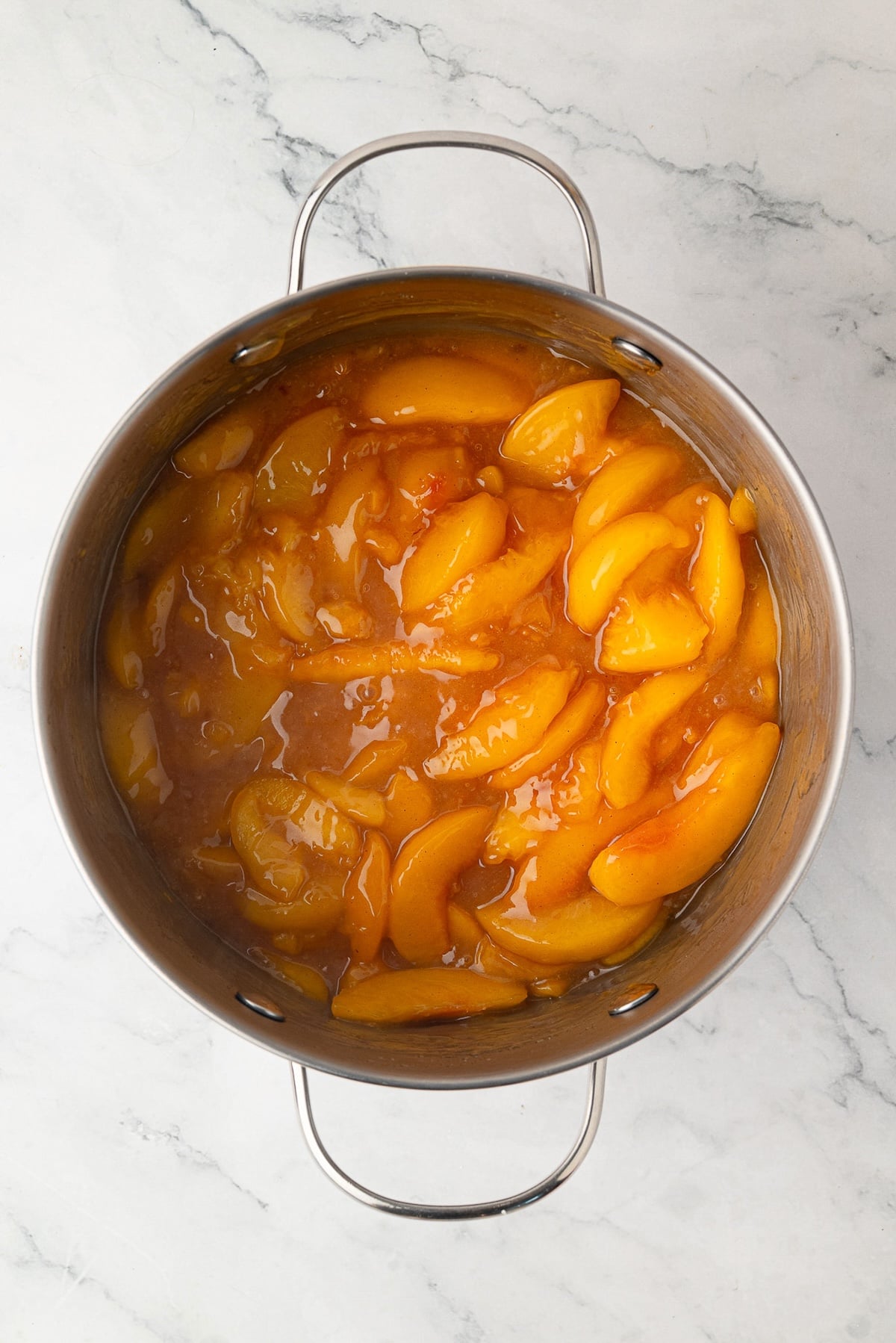 A close-up of thick, velvety precooked peach pie filling coated in a glossy syrup.