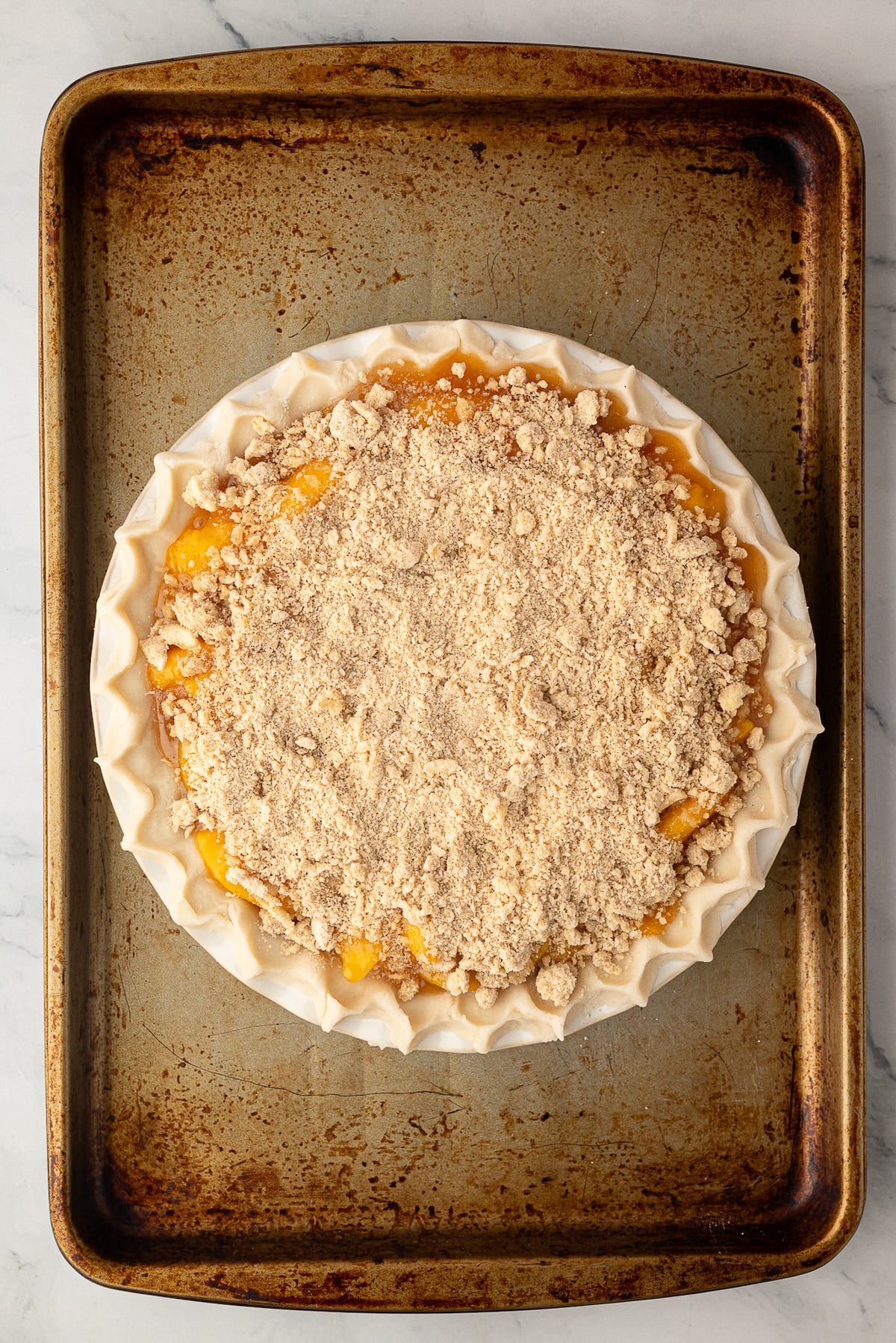 Deep-dish peach pie generously covered with a thick layer of butter crumb topping before baking.