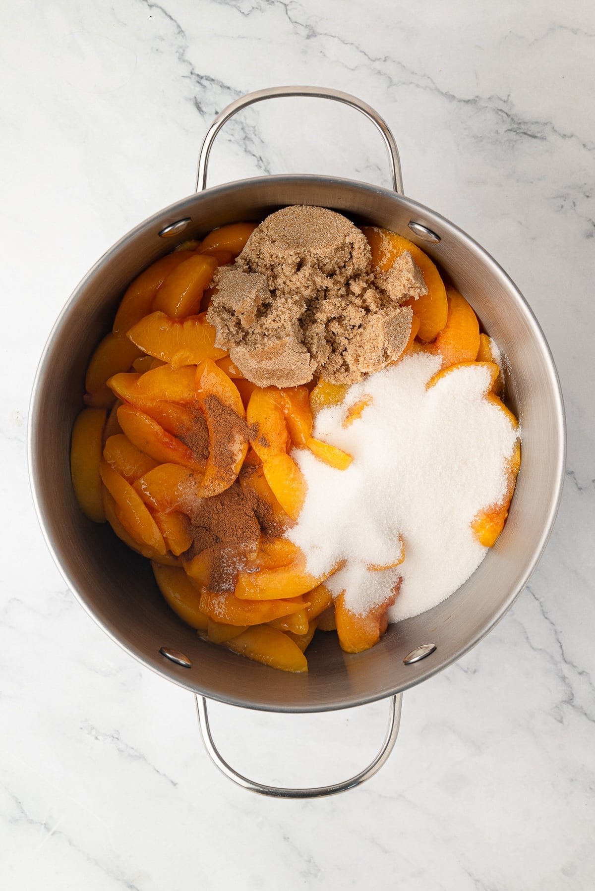Sliced peaches cooking with sugar and cinnamon in a large pot on the stovetop to make a thick pie filling.