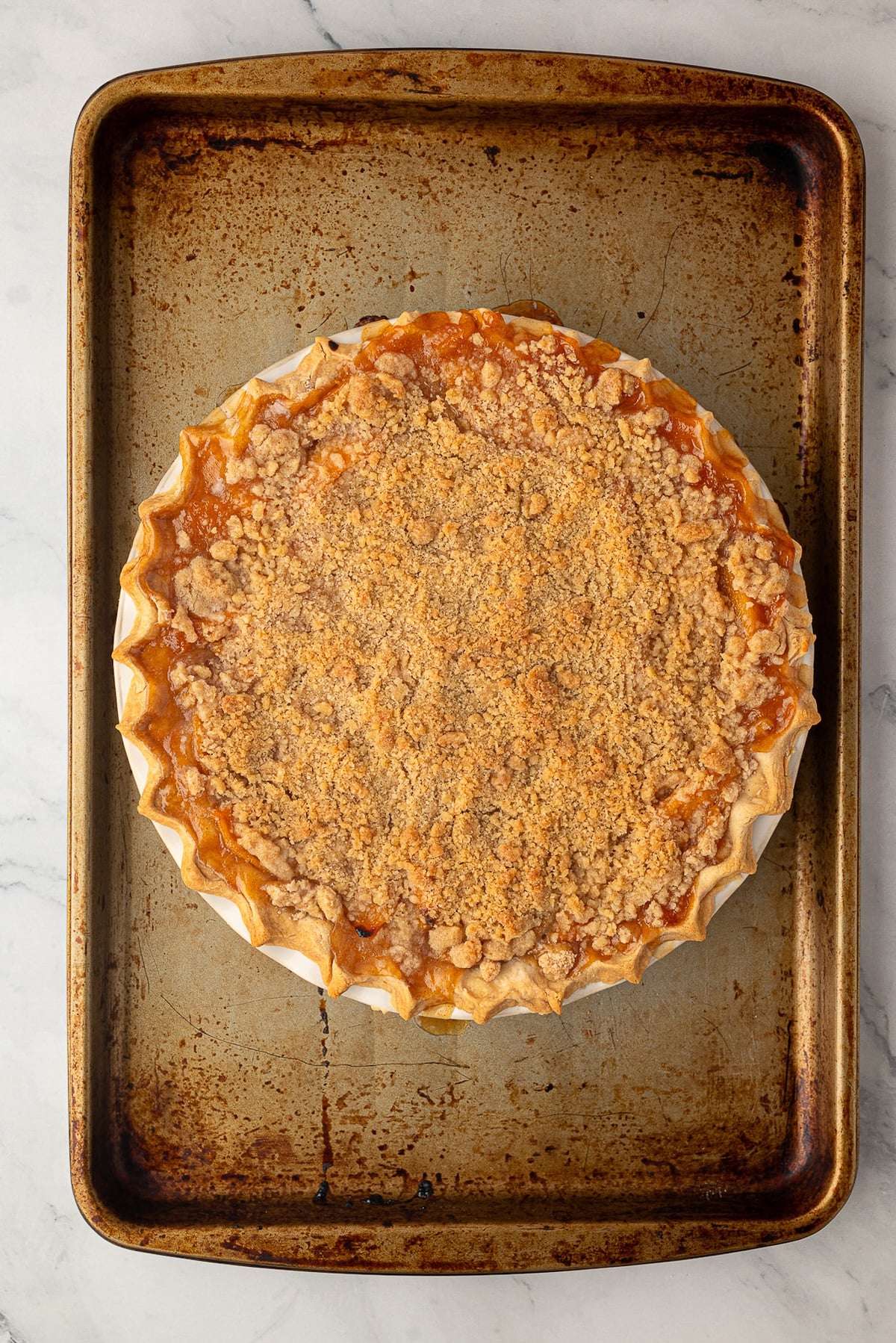 Peach pie placed on top of a baking sheet to catch any bubbling fruit juices.