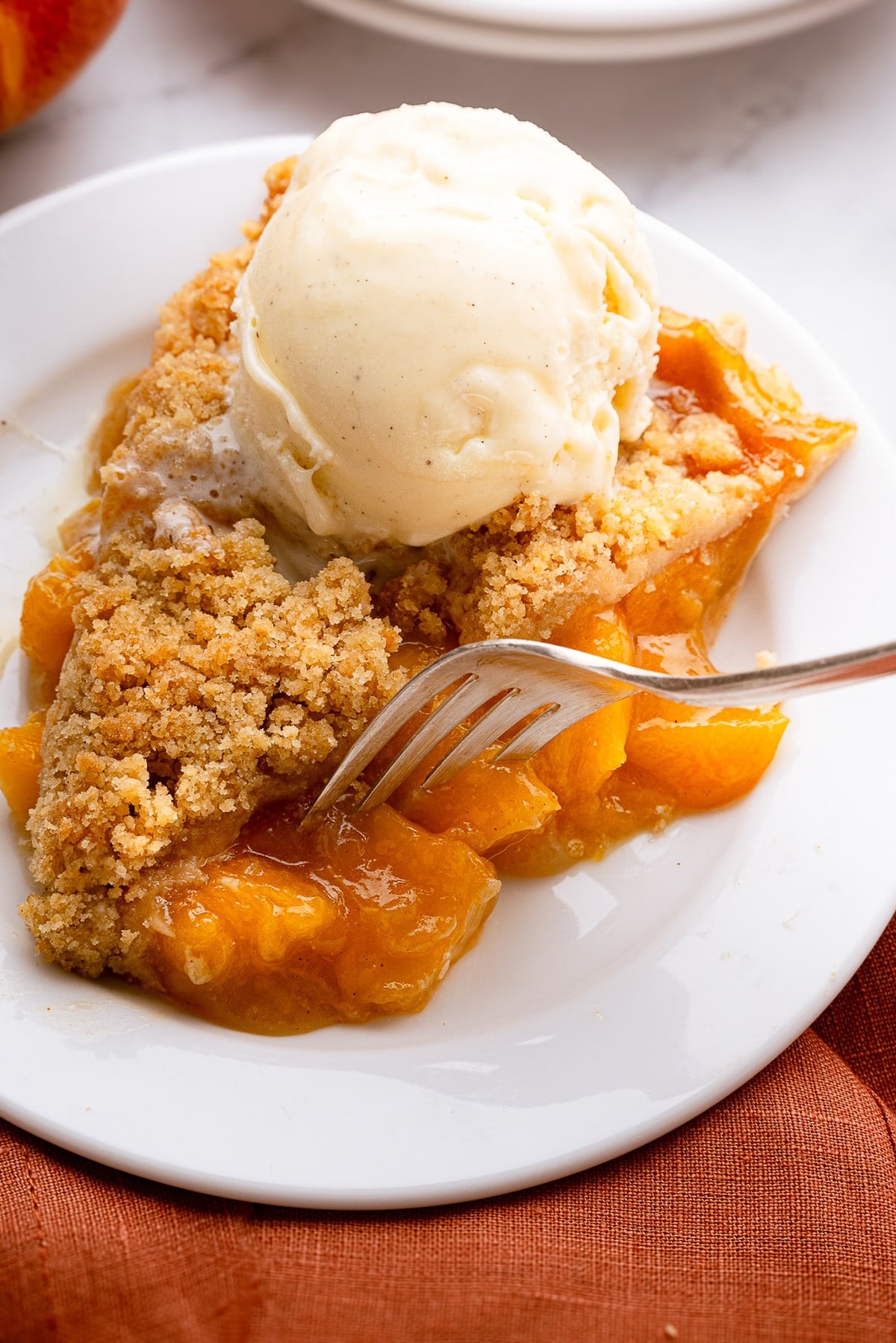A slice of warm deep-dish peach pie topped with a melting scoop of vanilla ice cream on a rustic dessert plate.
