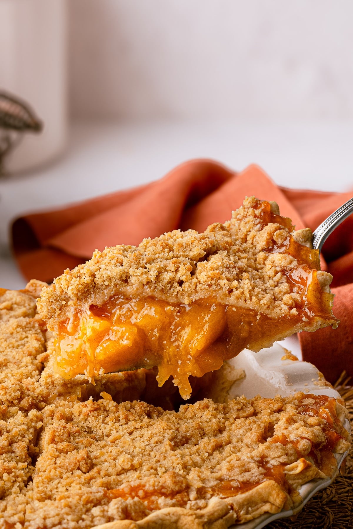 Slicing a deep dish peach pie, showing off a clear, velvety filling and a golden brown crumb topping.