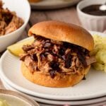 A slow cooker pineapple pulled pork sandwich on a toasted bun, layered with extra glossy BBQ sauce dripping down the sides.