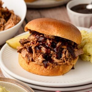 A slow cooker pineapple pulled pork sandwich on a toasted bun, layered with extra glossy BBQ sauce dripping down the sides.