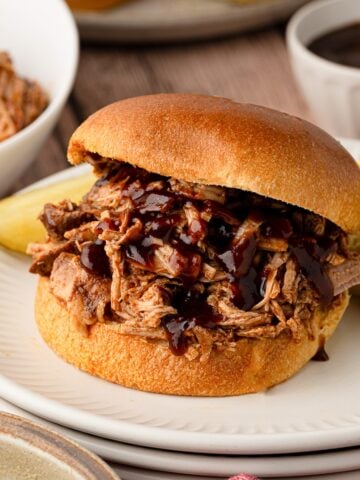 A slow cooker pineapple pulled pork sandwich on a toasted bun, layered with extra glossy BBQ sauce dripping down the sides.
