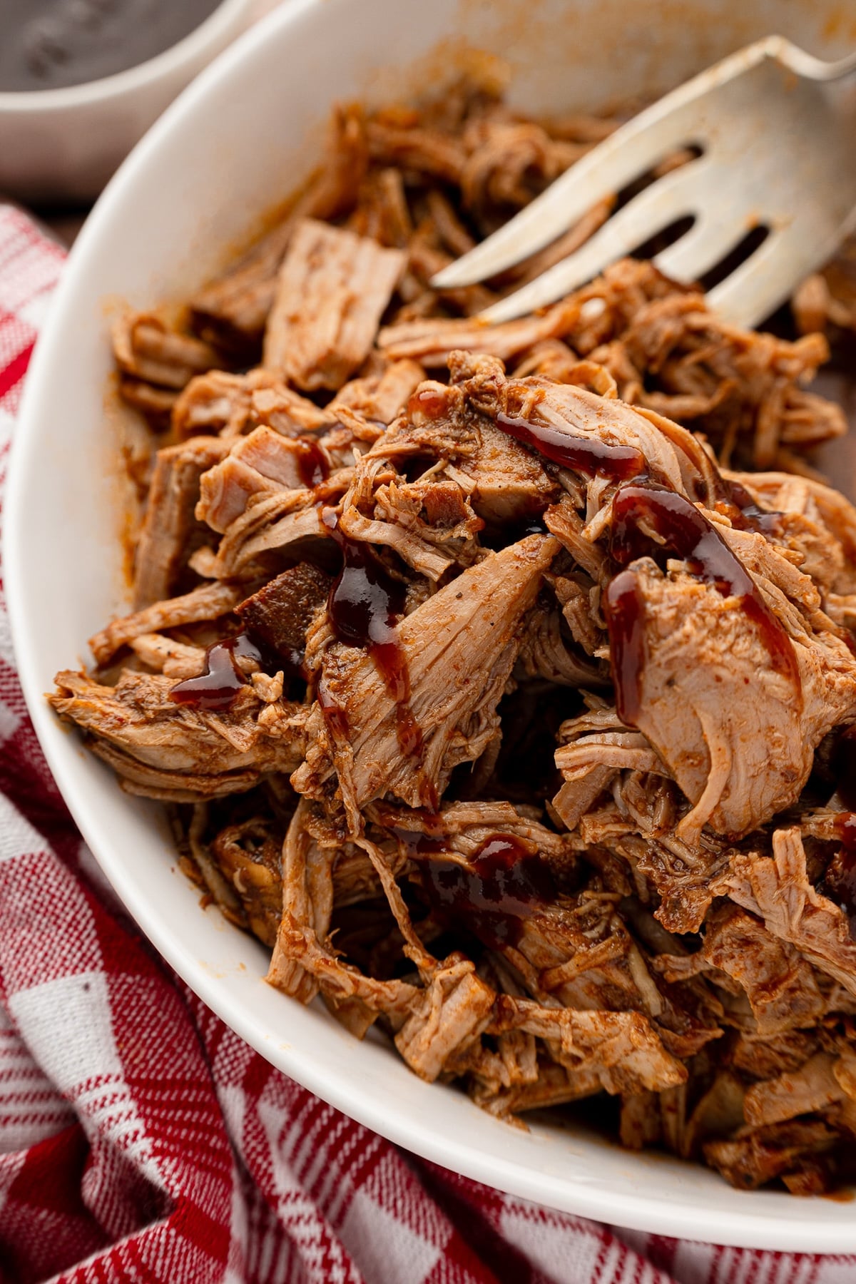 Shredded pork tenderloin in a serving bowl with extra barbecue sauce.