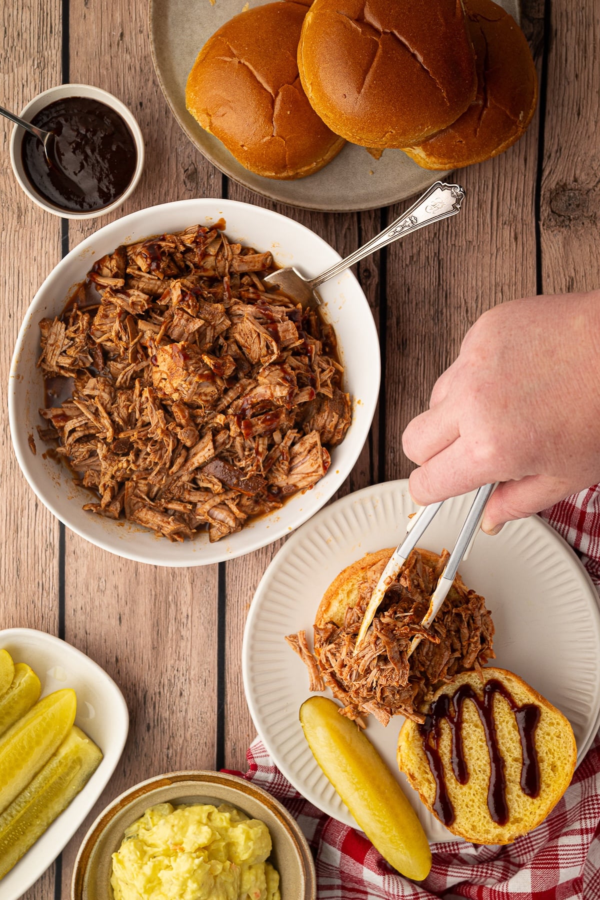 Topping buns with shredded pineapple pork, served with potato salad, pickles and extra BBQ sauce.
