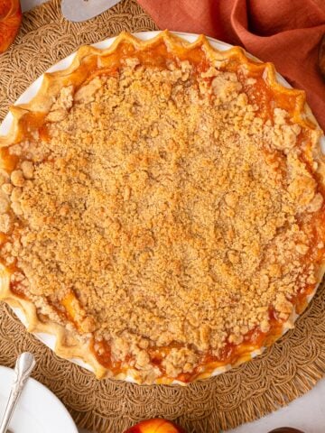 A whole homemade peach crumble pie fresh from the oven, featuring a golden-brown streusel topping and bubbling juices.