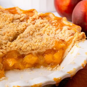 A golden-brown Texas peach crumble pie with a crisp, buttery streusel topping, served in a deep-dish pie plate, sliced showing a rich peach pie filling.