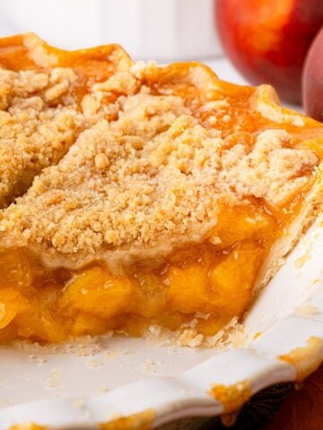A golden-brown Texas peach crumble pie with a crisp, buttery streusel topping, served in a deep-dish pie plate, sliced showing a rich peach pie filling.