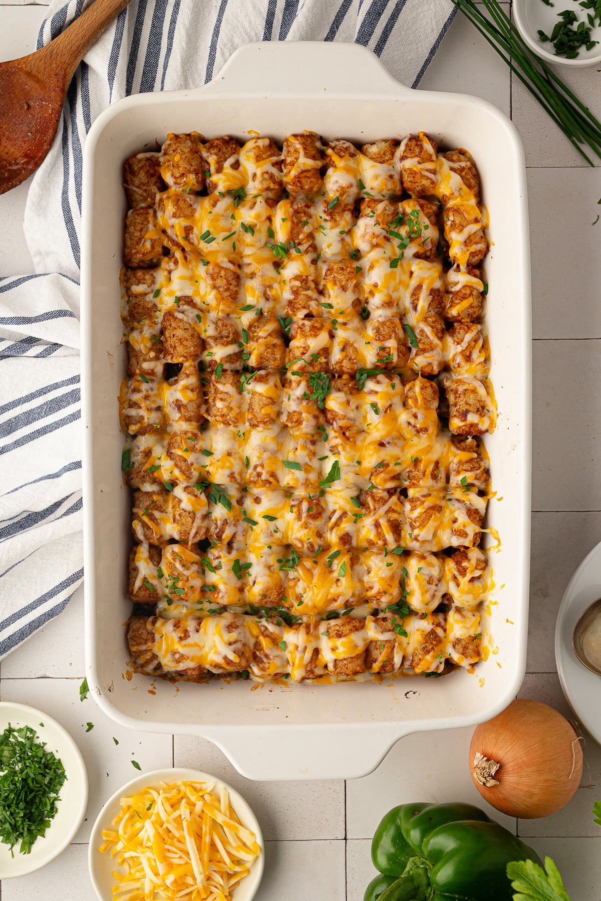 Golden-baked Sloppy Joe Tater Tot Casserole in a 9x13 white baking dish with melted cheddar cheese and a garnish of freshly chopped green onions.