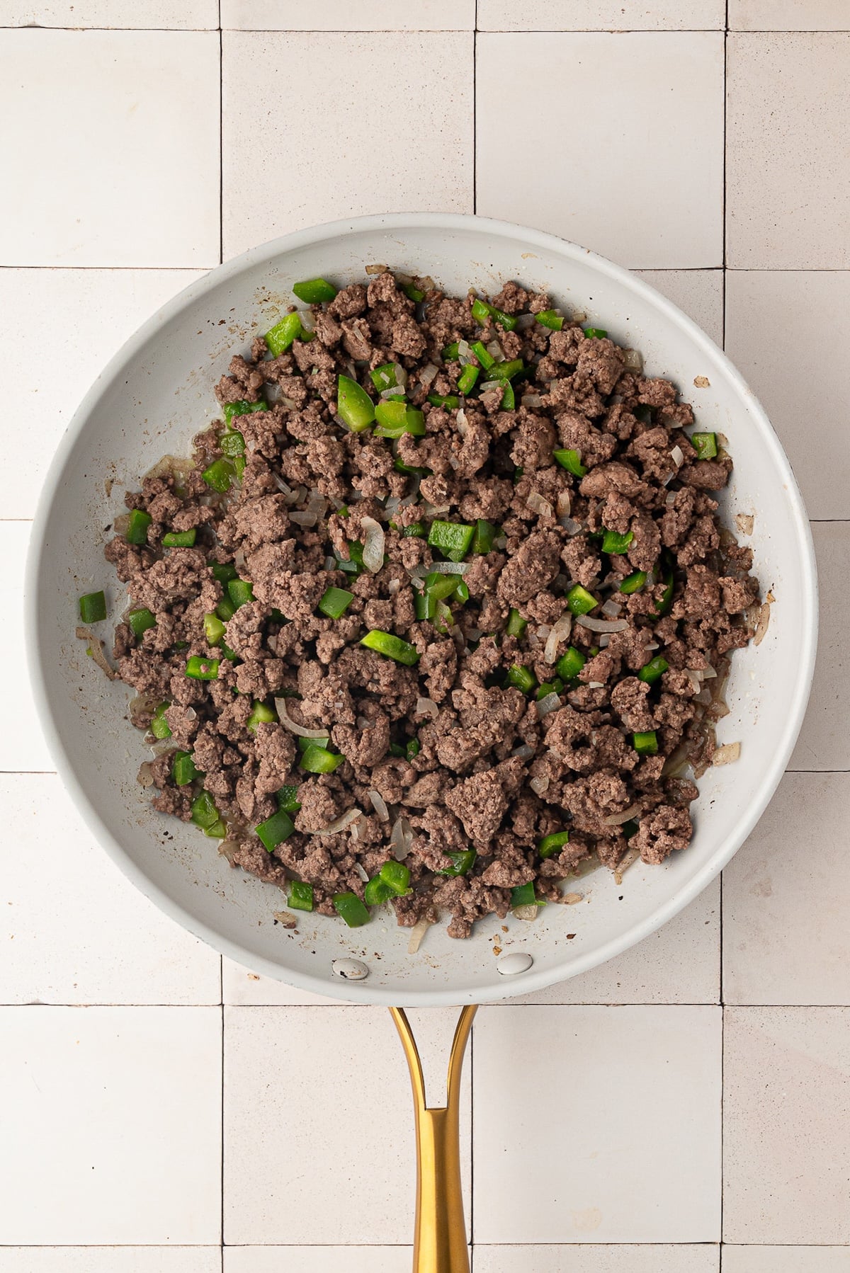 Browning lean ground beef in a skillet mixed with diced yellow onions and diced green bell peppers for a homemade sloppy joe base.