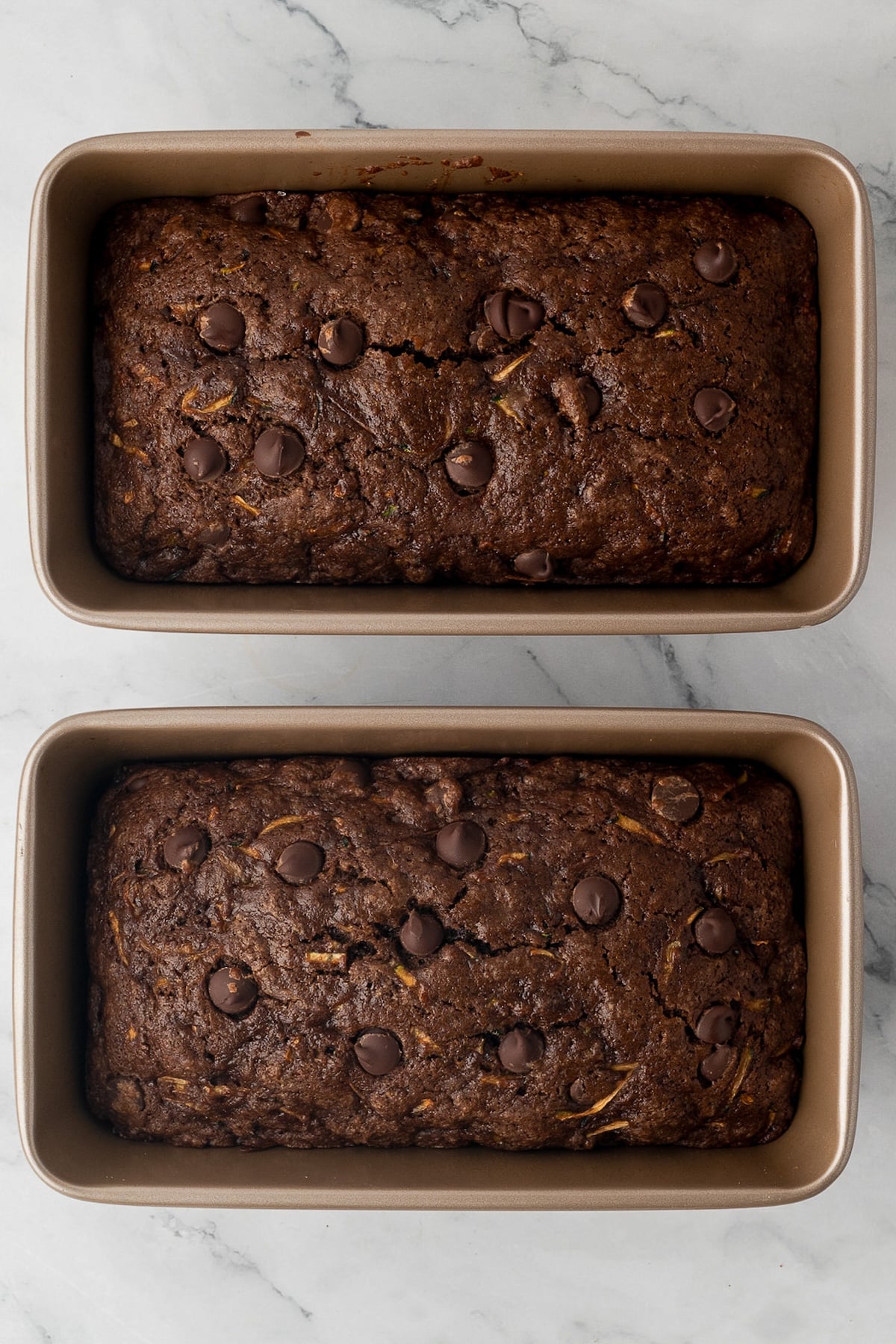 Two loaves of chocolate zucchini bread with chocolate chips fresh out of the oven in loaf pans.