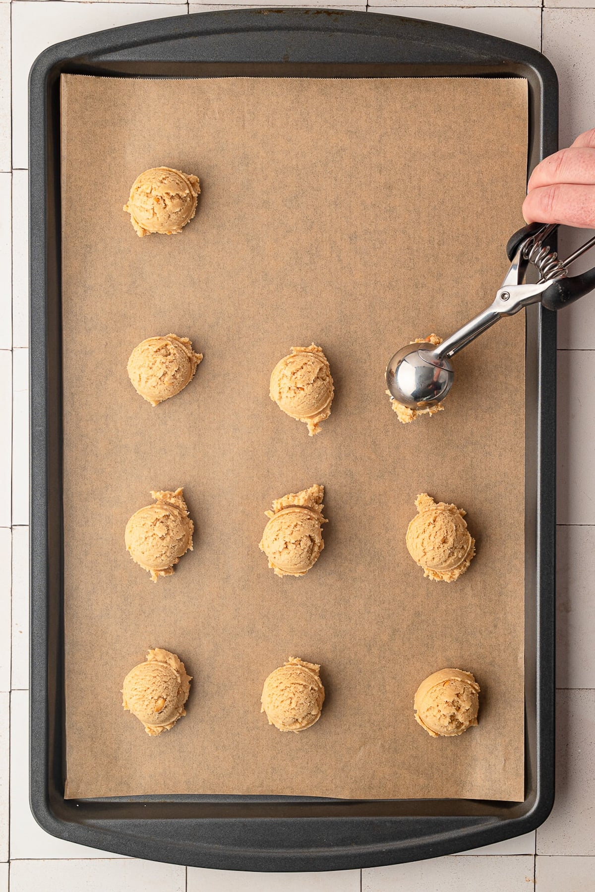 Using a cookie scoop to portion out peanut butter cookie dough on a lined baking sheet.