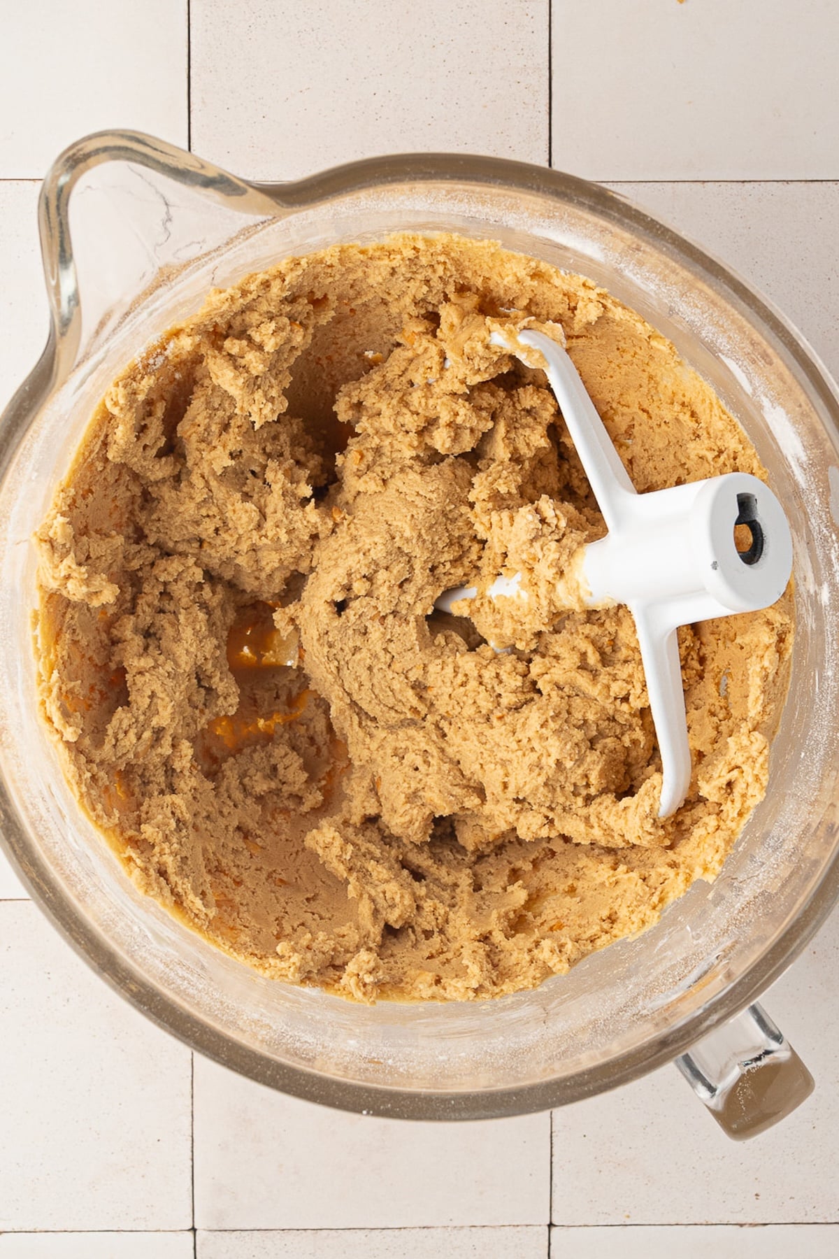 A mixing bowl full of peanut butter cookie dough, showing a thick texture with bits of peanuts from the crunchy peanut butter sprinkled throughout.