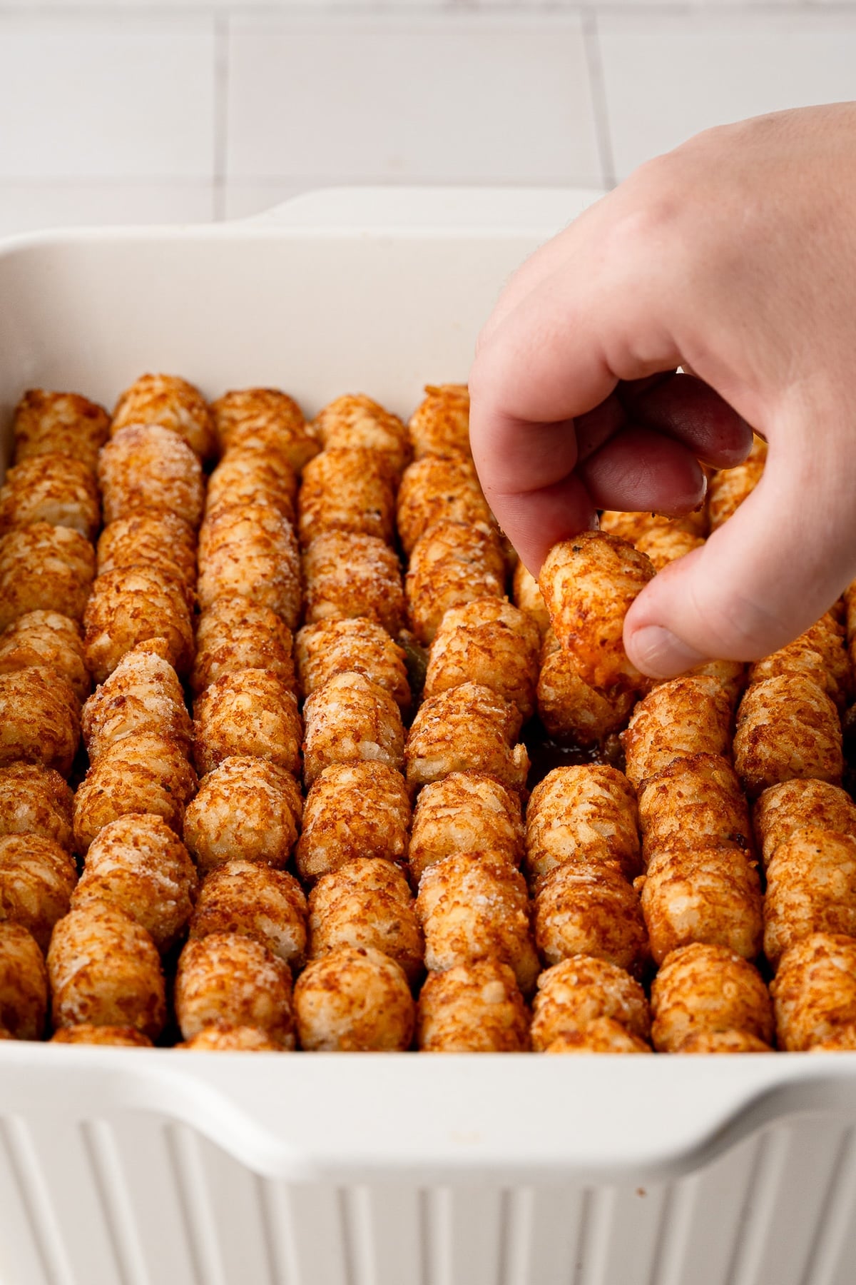 Arranging frozen tater tots in a neat single layer on top of the cooked sloppy joe meat mixture in a 9x13 baking dish.