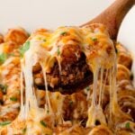 A wooden spoons scoops a layer of the Easy Sloppy Joe Tater Tot Casserole showing a rich ground beef base, crispy tater tots, and melty cheese.