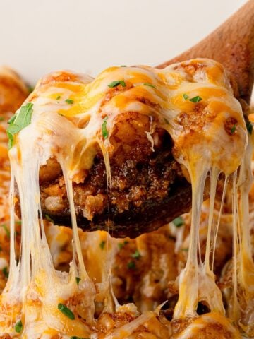 A wooden spoons scoops a layer of the Easy Sloppy Joe Tater Tot Casserole showing a rich ground beef base, crispy tater tots, and melty cheese.