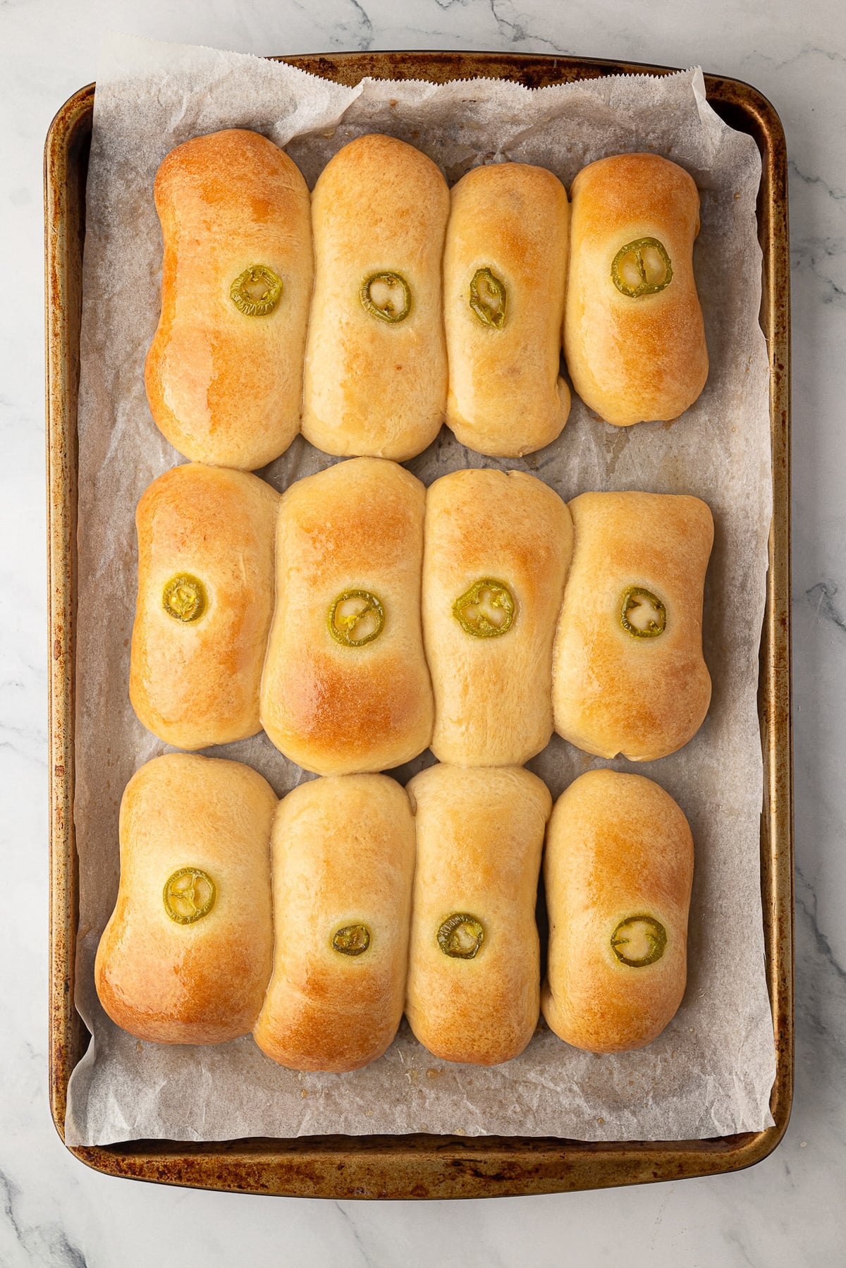 A dozen sausage cheese jalapeno kolaches on a baking sheet fresh out of the oven.