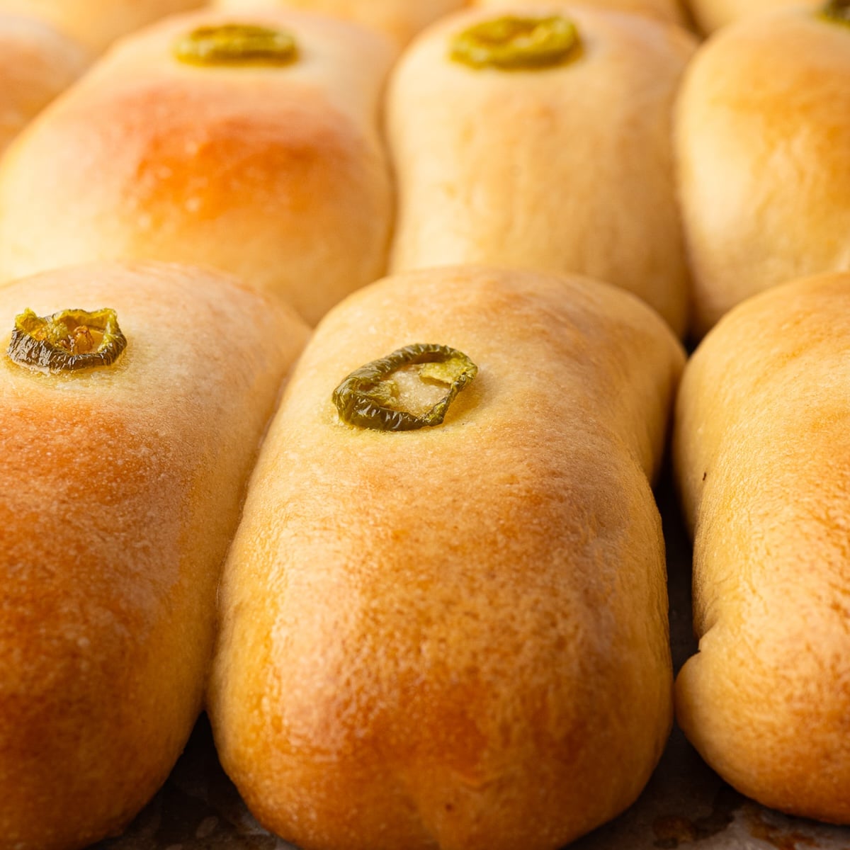 Golden brown, freshly baked jalapeno sausage cheese kolaches with jalapeno ring on top.