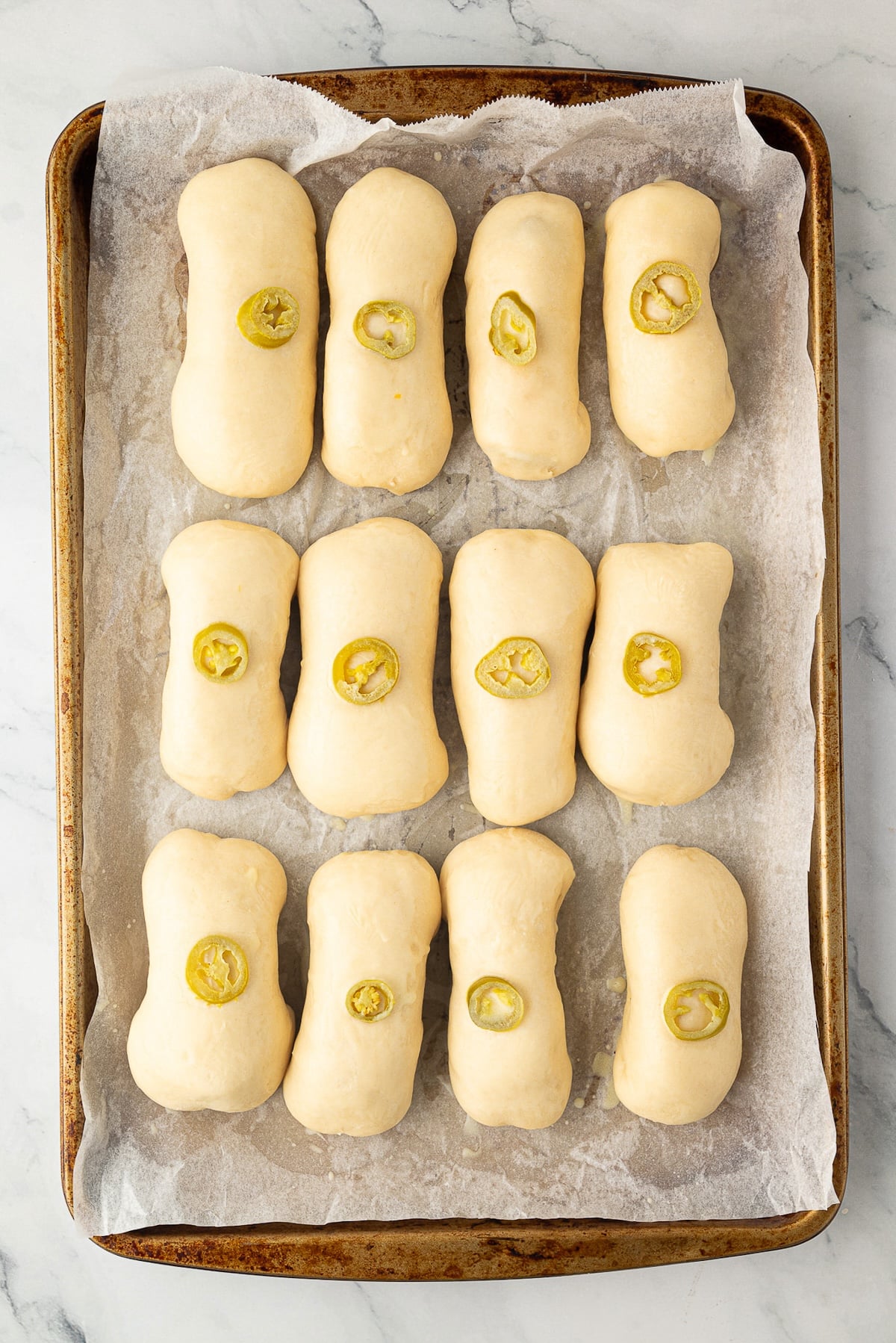 A baking sheet of a dozen jalapeno sausage cheese kolaches looking puffy after the second rise.